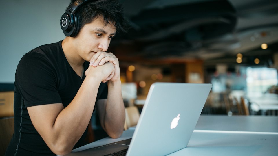Mann mit Kopfhörern schaut auf seinen Laptop